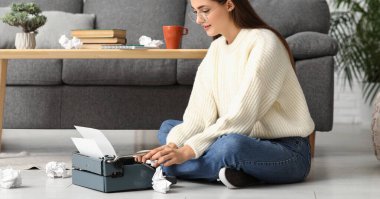 Daktilo ve buruşuk kağıt çarşaflarla evde oturan kadın yazar.