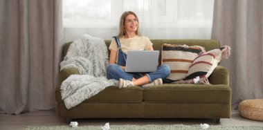 Evde kanepede oturan dizüstü bilgisayarı olan bir kadın yazar.