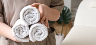 Kadın masaj terapisti spa salonunda temiz havlu tutuyor, yakın plan.