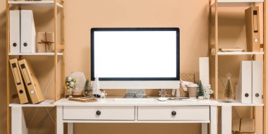 Ofiste bej duvarın yanında bilgisayar ve Noel dekoru olan bir işyeri