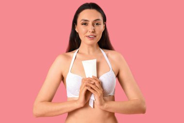 Pembe arka planda güneş kremi sürmüş genç bir kadın.