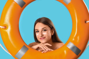 Mavi arka planda güneş kremi olan genç bir kadın.