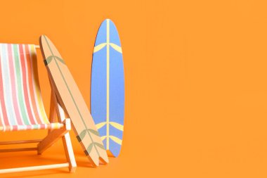 Turuncu arka planda mini sörf tahtaları ve şezlonglu kompozisyon