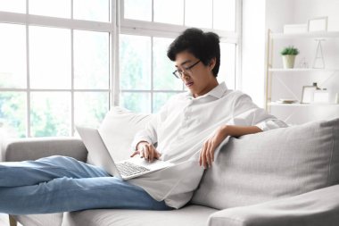 Genç Asyalı adam izin gününde dizüstü bilgisayar kullanıyor.