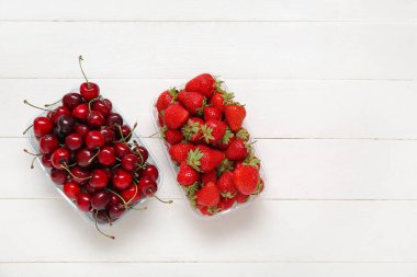 Hafif ahşap arka planda taze çilek ve kirazlı plastik kaplar.