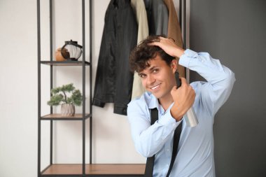 Yakışıklı genç adam koridordaki kıvırcık saçlarına saç spreyi sıkıyor.