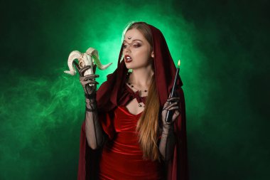 Koyu yeşil arka planda mum ve koyun kafatası ile güzel genç cadı