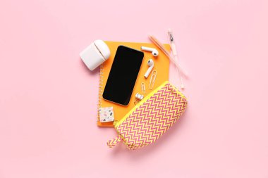 Pembe arka planda cep telefonu ve kulaklığı olan kırtasiye malzemesi