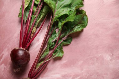 Pembe arka planda yeşil yapraklı taze pancarlar.