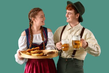 Geleneksel Alman elbiseli genç çift yeşil arka planda bira ve atıştırmalıklarla