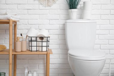 Tuvalet deliğinin yanındaki raflarda kağıt rulo ve banyo malzemeleri olan sepet.