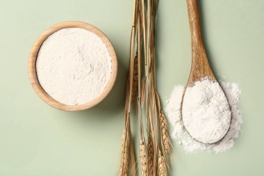 Bowl and spoon with wheat flour on green background