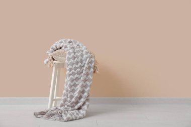 Yastıklı tabure ve bej duvarın yanında rahat battaniye