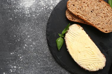 Board of tasty toast with butter and basil on grey background