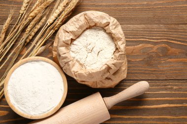 Tahta arka planda buğday kulaklı kağıt torba ve bir kase un.