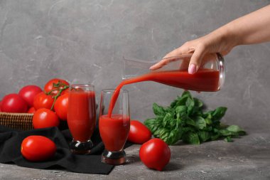 Gri arka planda sürahiden bardaklara lezzetli domates suyu döken kadın.