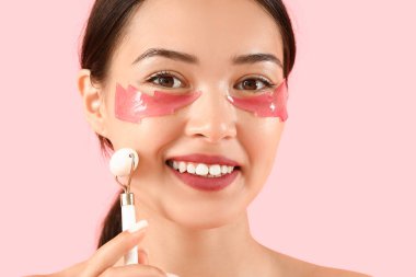 Göz altı bantları ve pembe arka planda yüz masajı yapan güzel bir kadın.