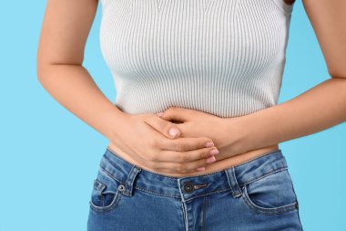 Mavi arka planda karın ağrısından muzdarip güzel bir kadın, yakın plan.