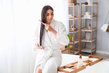 Güzel genç bir kadın banyoda saçına hindistan cevizi yağı sürüyor.