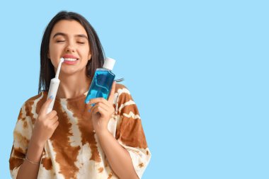 Elektrikli diş fırçası ve ağzı mavi arka planda durulanmış gülümseyen genç kadın.