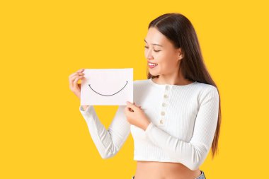 Sarı arka planda kağıt gülüşlü genç Asyalı kadın.