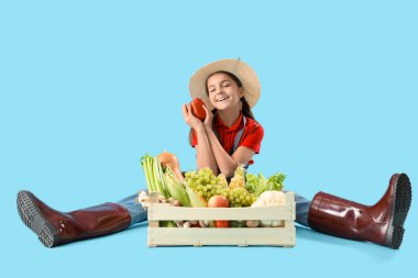 Mavi arka planda oturan taze yiyecekli küçük çiftçi.