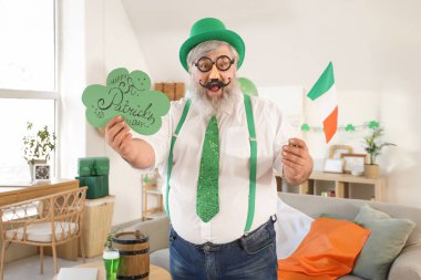 Aziz Patrick Günü 'nde evde kart ve İrlanda bayrağı taşıyan komik kılık değiştirmiş olgun bir adam.