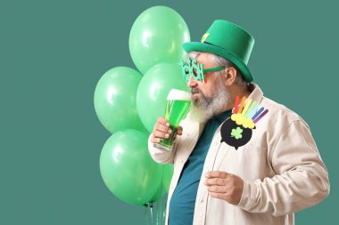 Yeşil arka planda bira ve dekor olan olgun bir adam. Aziz Patrick Günü kutlaması
