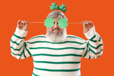 Turuncu arka planda kağıt yoncaları olan olgun bir adam. Aziz Patrick Günü kutlaması