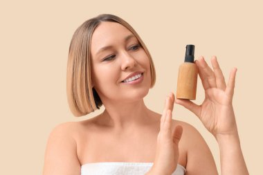 Güzel olgun bir kadın arka planda kozmetik ürünü şişesi tutuyor.