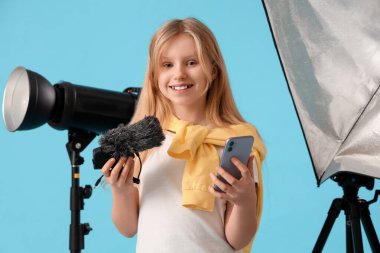 Mavi arka planda mikrofonu ve cep telefonu olan genç blogcu