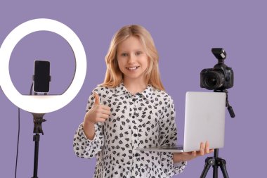 Modern dizüstü bilgisayarı, fotoğraf makinesi ve eflatun arkaplanda halka ışığı olan genç blog yazarı
