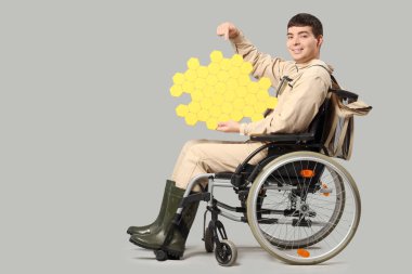 Male beekeeper in wheelchair with paper honeycombs on light background clipart