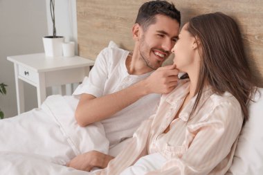 Yatakta uzanmış gülümseyen genç çift.