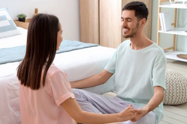 Genç çift el ele tutuşuyor ve yatağın yanında oturuyor.