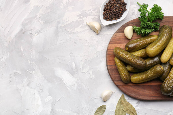 Wooden board with pickled cucumbers and different spices on grey background