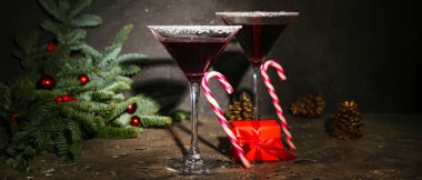 Lezzetli kırmızı margarita bardakları, hediye, baston şekerler ve karanlık arka planda duran Noel dekoru.