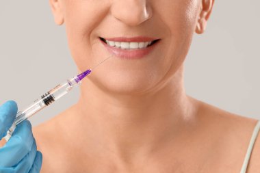 Olgun kadın ışık arka planında doldurucu enjeksiyon alıyor