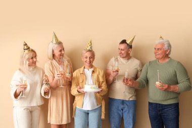 Pasta ve şampanyayla olgun insanlar bej arka planda doğum gününü kutluyorlar.