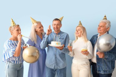 Pasta ve balonla olgun insanlar mavi arka planda doğum gününü kutluyorlar.