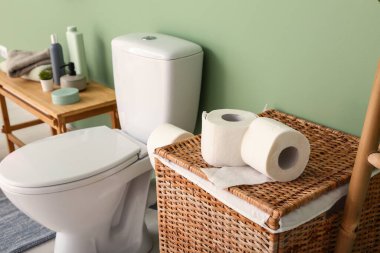 Renk duvarının yanında tuvalet kağıdı, klozet ve kozmetik ürünleri olan çamaşır sepeti, yakın plan.