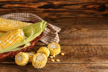 Tahta arka planda taze mısır koçanları olan sepet.