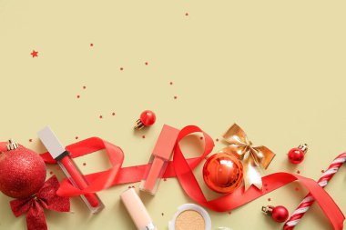 Dekoratif kozmetik ürünleri ve açık sarı arka planda kırmızı Noel dekoru olan kompozisyon