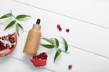 Temel yağ, nar ve bitki yapraklarıyla hafif ahşap zemin üzerinde bileşim