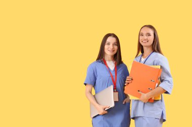 Dizüstü bilgisayarı ve sarı arka planda klasörleri olan kadın tıp öğrencileri.