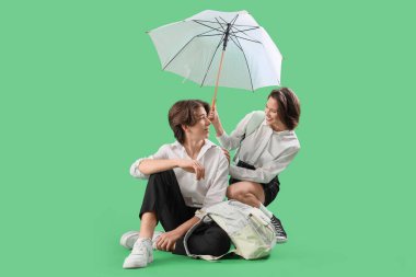 Yeşil arka planda şemsiyesi olan birkaç öğrenci.