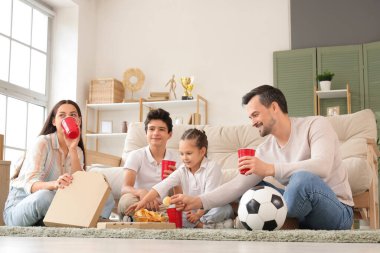 Evde futbol maçı izleyen mutlu bir aile, içki ve abur cubur.