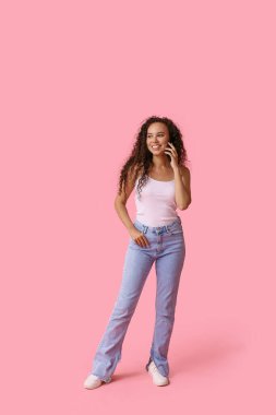 Pembe arka planda cep telefonuyla konuşan mutlu Afro-Amerikan kadın.