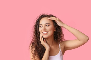 Pembe arka planda sağlıklı nemlendirilmiş cilde sahip mutlu genç Afro-Amerikan kadın.