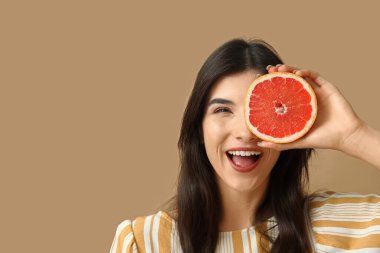 Güzel bir genç kadın bir gözünü bej arka planda greyfurtla kaplıyor.